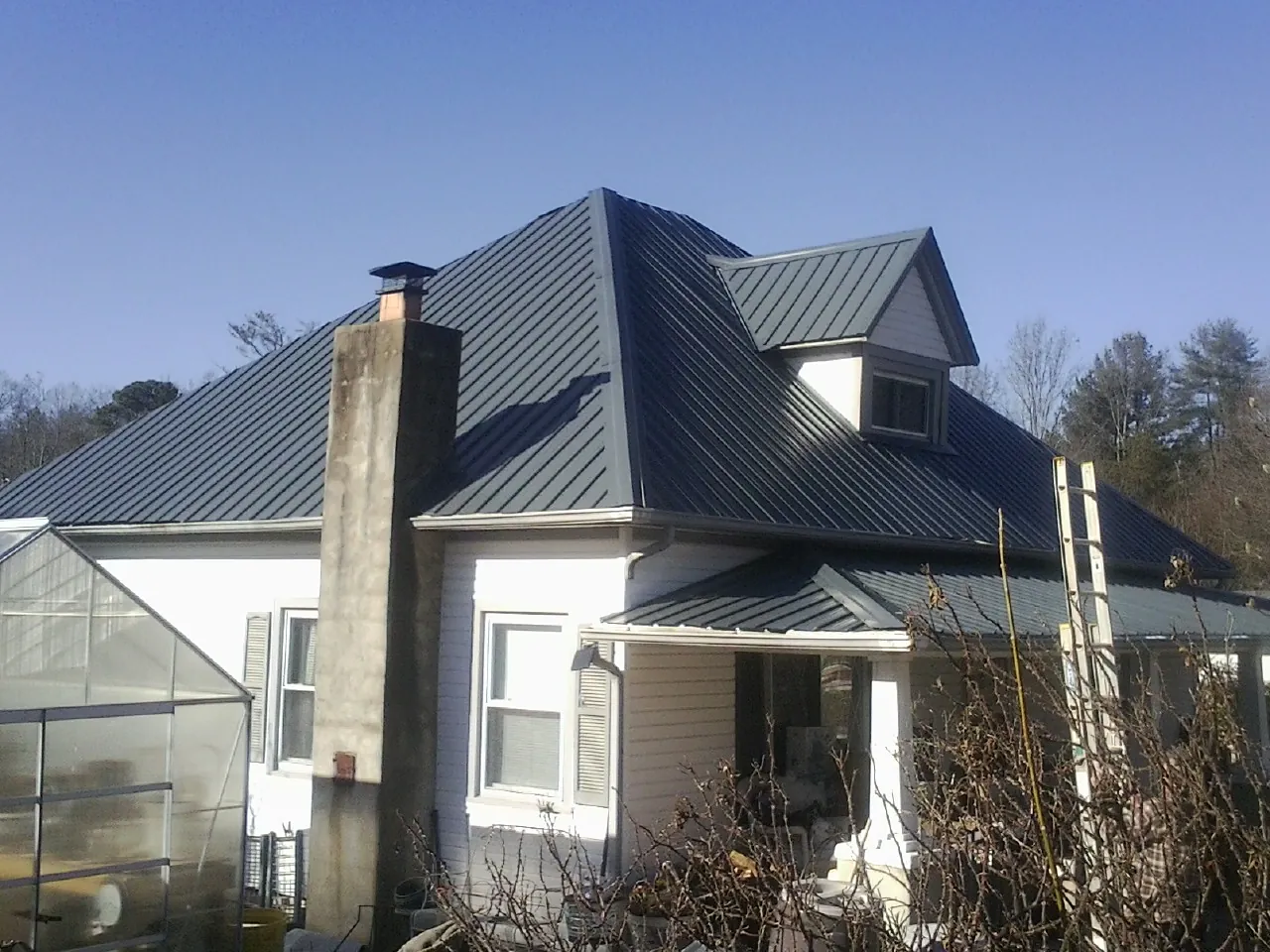 Dark blue standing seam metal roof on a white farmhouse with dormer — Slate & Tile Roof Repair by Roofing Brothers in Johnsonville