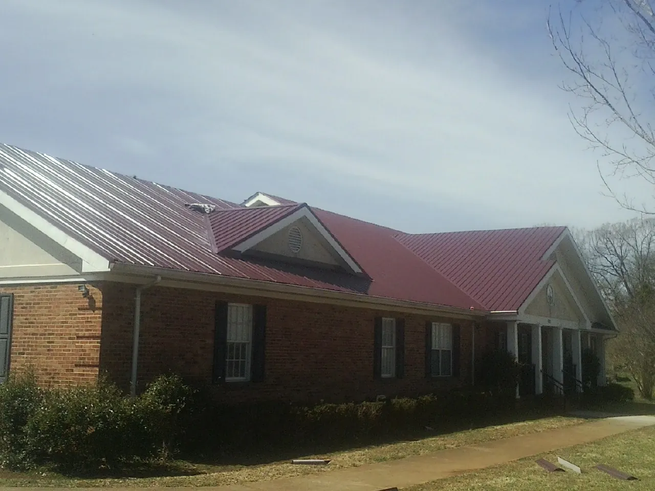 Red metal roof with gabled entries on a long brick building, from a Hail Damage Roof Repair job in Johnsonville