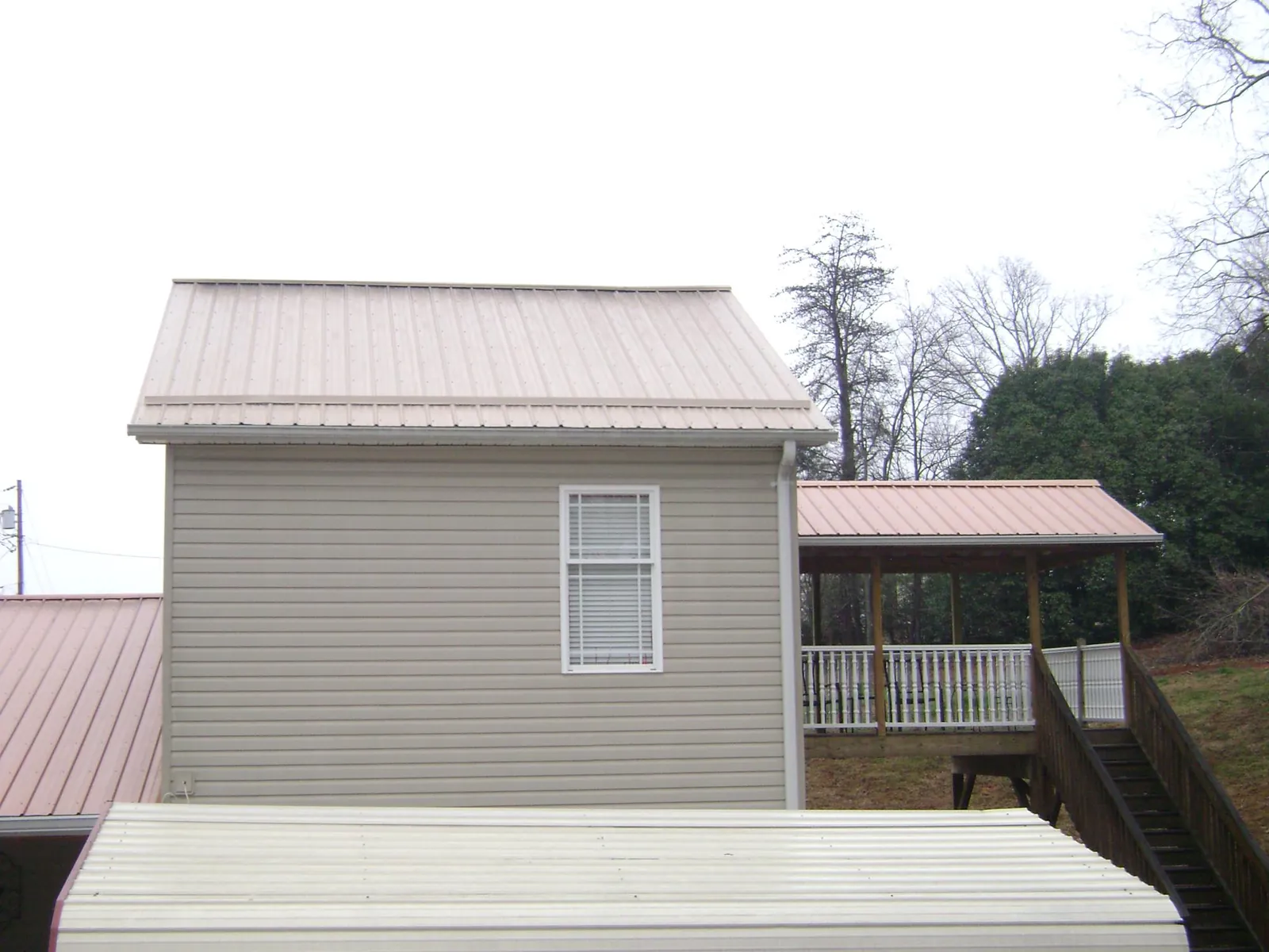 Tan metal roofs on a two story addition and attached porch, from a Roof Replacement job in Johnsonville